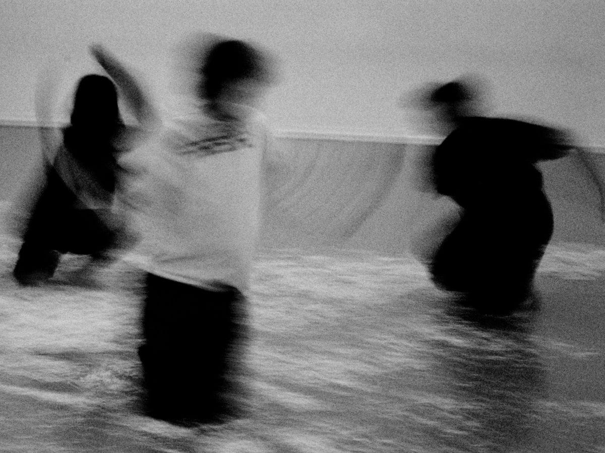 Three dancers kneel on the floor of a studio, surrounded by shredded paper. They perform in Stasiland, by choreographer Olivia Wallis Jackson